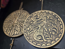 Load image into Gallery viewer, Bronze medallion with intricate design of a creature and floral elements on a dark background